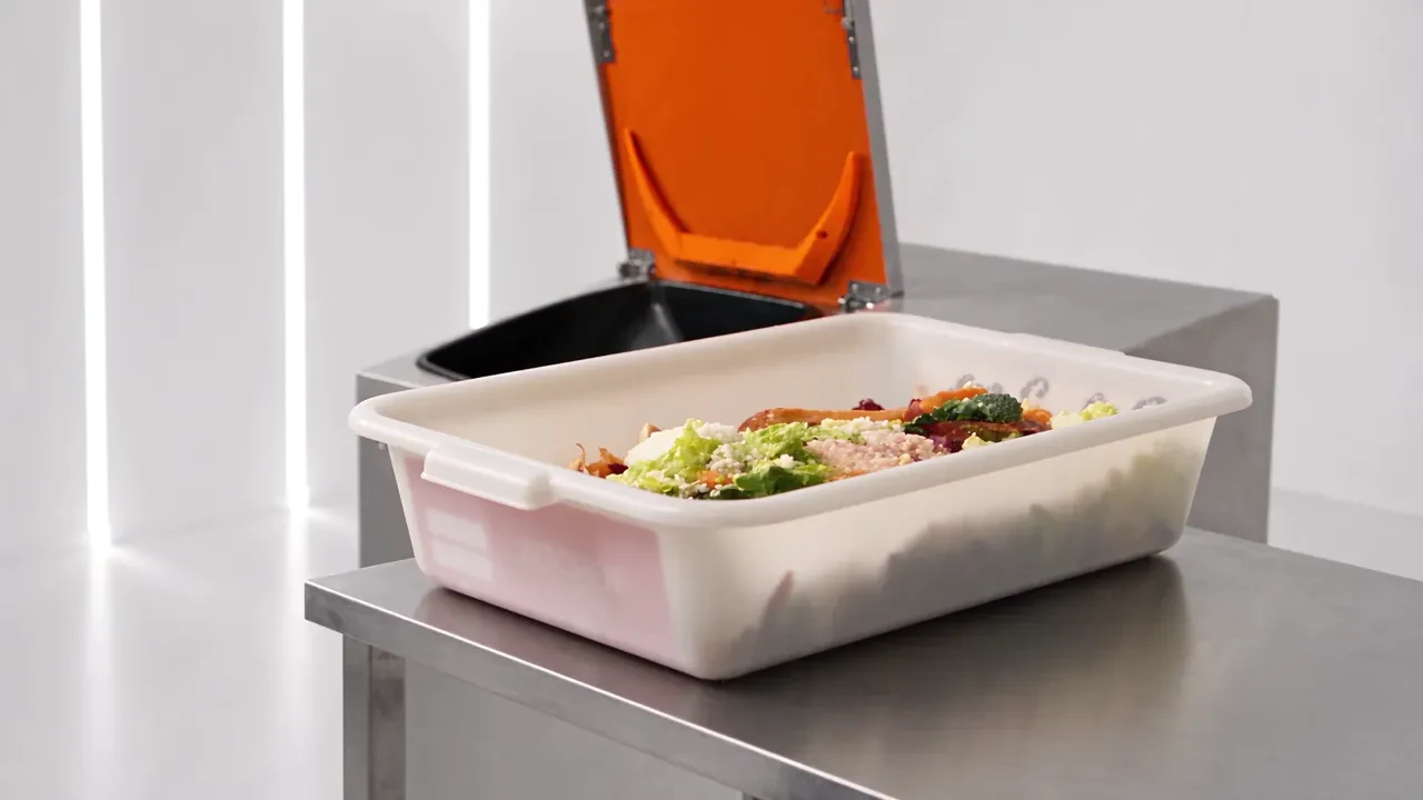 One unbranded white bin of food scraps on a stainless steel table in a clean commercial kitchen